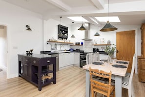 A modern kitchen with white cabinets, a dark wooden island, pendant lights, and a dining area with a table set for two. - Sidlesham Hideaway Logburner Garden (Chichester)