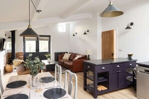 A modern kitchen with a dark island, white chairs, and a dining table set for four. - Sidlesham Hideaway Logburner Garden (Chichester)