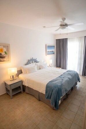 A hotel room with a bed, nightstands, a ceiling fan, and a window with curtains. - Altos De Cabrera Village (Cabrera)