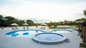 En swimmingpool med ett bubbelbad, solstolar och parasoller.