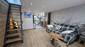 Ein modernes Wohnzimmer mit einer Holztreppe, einem Karomuster-Sofa und einer Küche im Hintergrund.