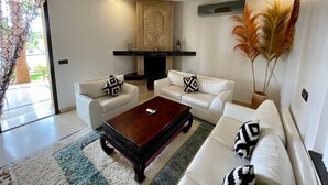 A modern living room with white sofas, a wooden coffee table, and a decorative wall panel. - Luxury villa heated pool (Marrakech)