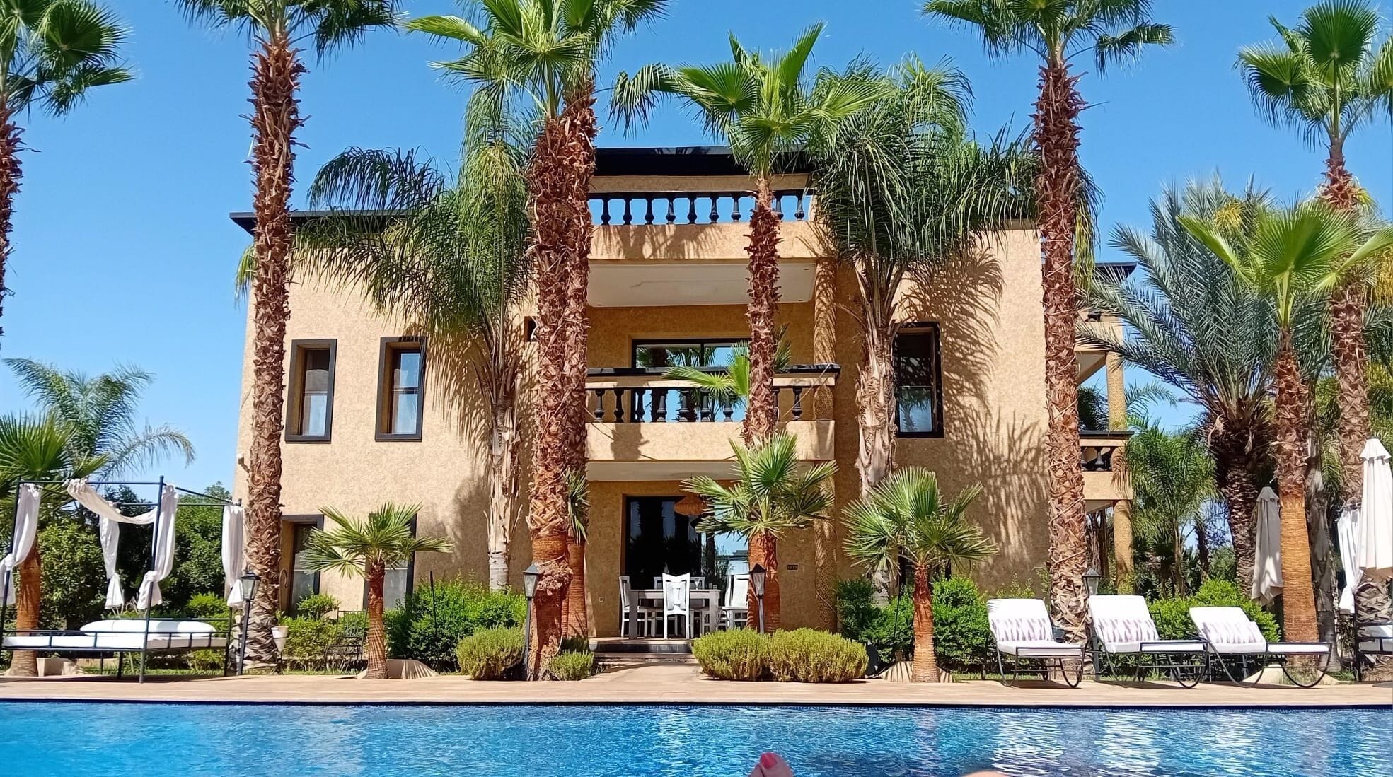 A hotel with a pool, palm trees, and a two-story building with balconies.