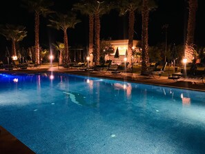 A nighttime swimming pool with lounge chairs and palm trees, surrounded by a building with warm lighting. - Luxury villa with a heated pool (Marrakech)