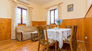 Una habitació acollidora amb terra de fusta, un sofà, una taula de dinar amb cadires i dues finestres amb cortines.