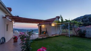 Zona d'estar a l'aire lliure coberta, amb una cadira bressol, una piscina i vista al mar.