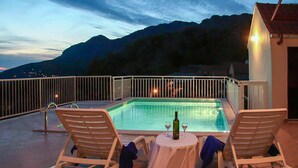 Piscina al terrat amb dues gandules i una taula, amb vista a un paisatge de muntanyes al capvespre.