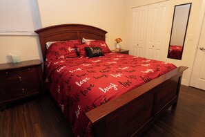 Quarto com uma cama de madeira, mesa de cabeceira, cômoda, espelho e porta.