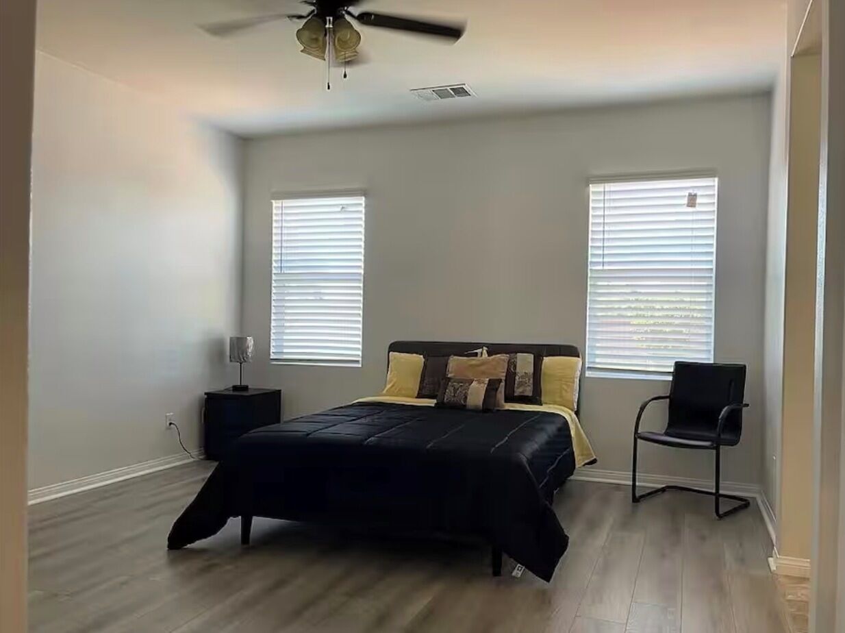 A bedroom with a bed, two windows, a chair, and a ceiling fan.