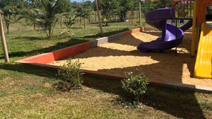 Un parque infantil con zona de juegos de arena, un tobogán morado y un tobogán amarillo, todo bajo un toldo grande.