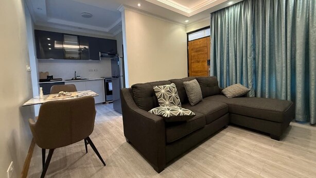 Una sala moderna con un sofá seccional, una mesa de comedor con sillas y una cocina al fondo.