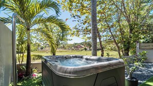 Un jacuzzi dans un jardin agrémenté de palmiers, avec une maison en arrière-plan.