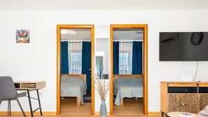 A room with two beds, a desk, a chair, a TV, and a decorative vase.