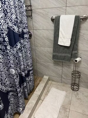 A bathroom with a patterned bathrobe hanging, a towel rack with a towel, and a metal towel rack with a towel. - Two bedrooms close to Plaza Las Americas (San Juan)