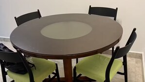 Een ronde eettafel met een glazen blad, omringd door vier stoelen met groene kussens.