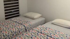 Een slaapkamer met twee bedden, een plafondventilator, een verwarming en een raam met jaloezieën.