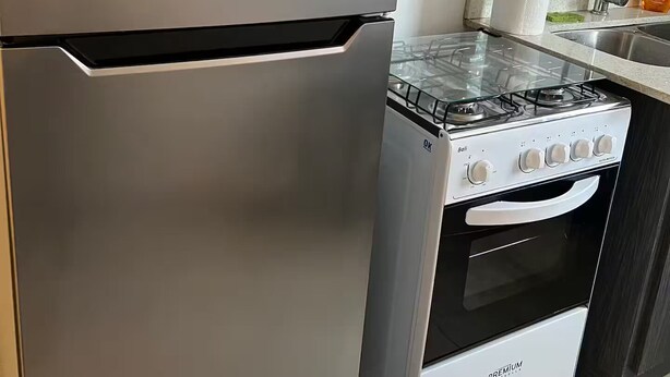 Een keuken met een roestvrijstalen koelkast, een gasfornuis en een oven. Op de koelkast zit een geel label met tekst en een prijs.