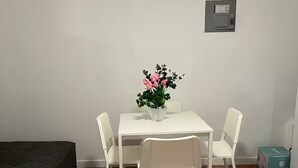 A small, modern room with a white table and four chairs, a potted plant with pink flowers, a grey electrical box on the wall, and a grey sofa. - 2 bedrooms in Hato Rey (San Juan)