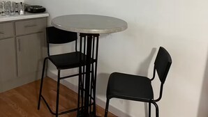 Una piccola cucina con un tavolo rotondo e due sedie, un piano di lavoro con bicchieri e una macchina del caffè, e pavimento in legno.