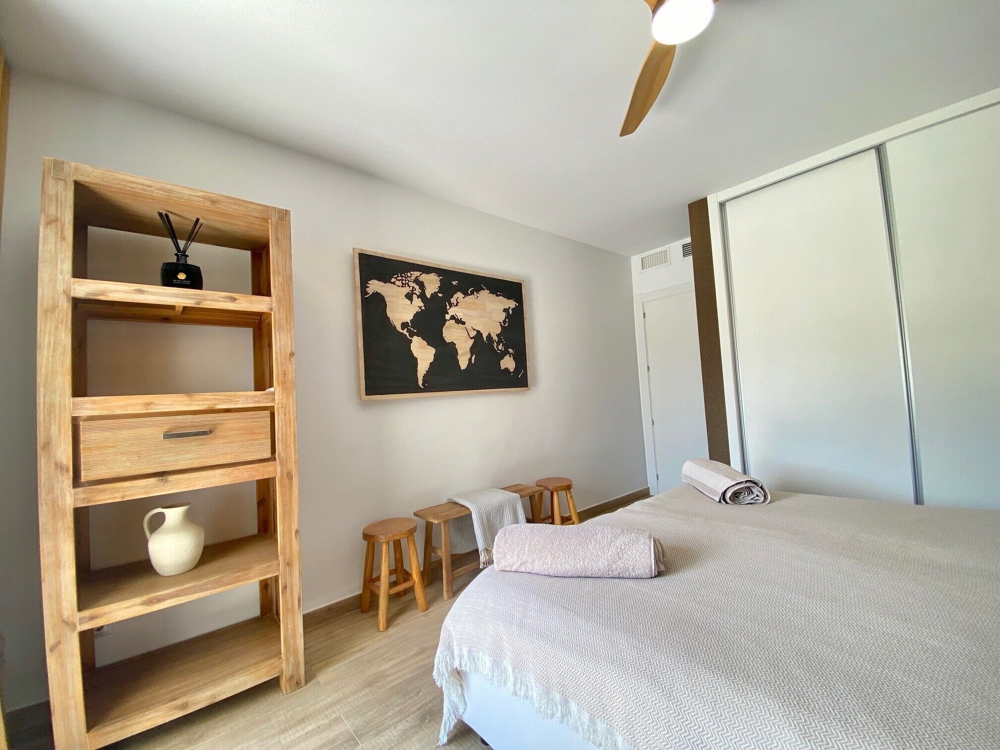 A bedroom with a bed, a wooden shelf unit, a world map, and a ceiling fan.