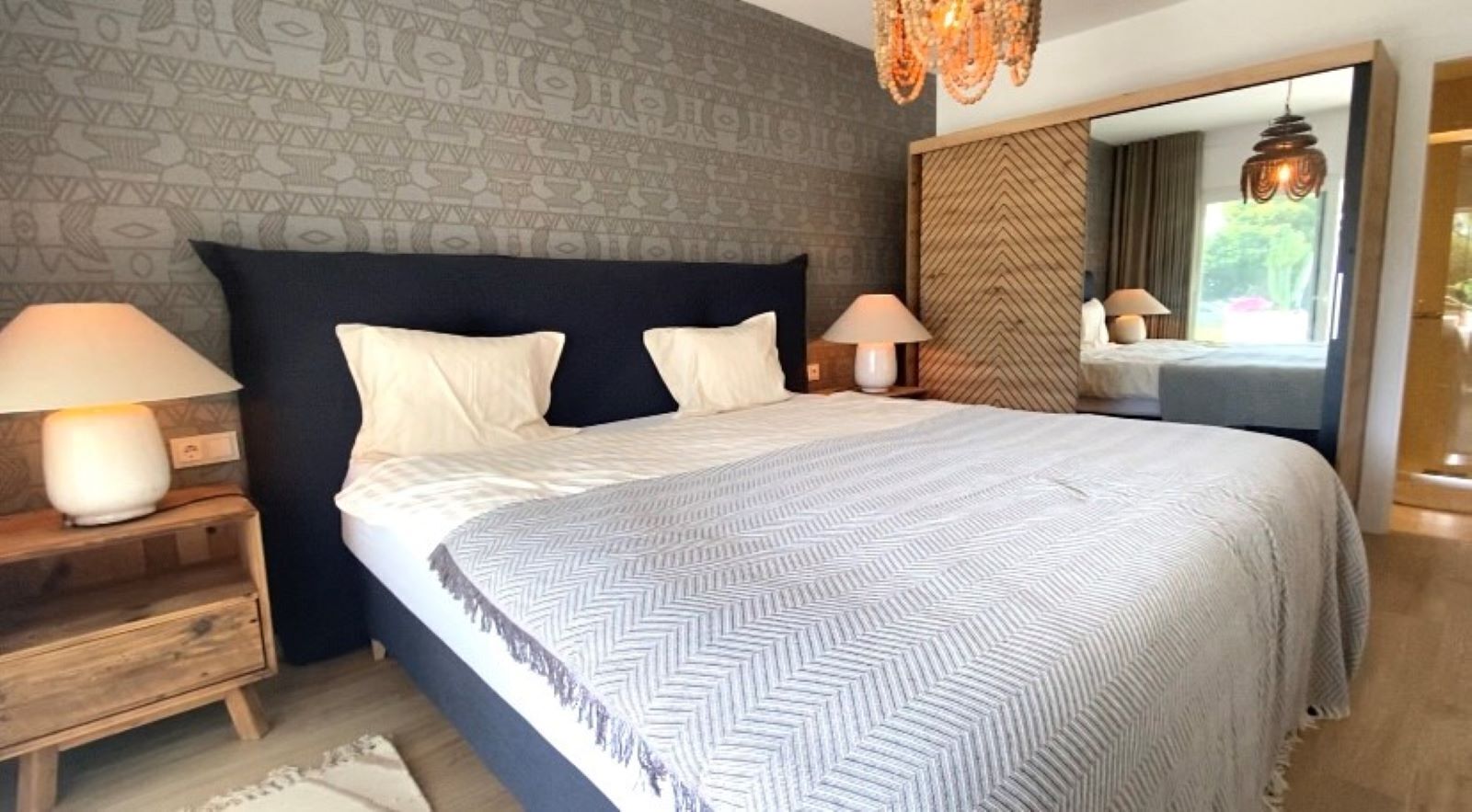 Un dormitorio con una cama grande, dos lámparas de noche, un espejo y una pared con diseño.