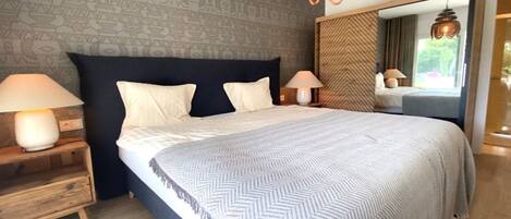 Ein Schlafzimmer mit einem großen Bett, zwei Nachttischlampen, einem Spiegel und einer Wand mit Muster.
