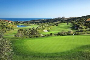 A golf course with a flagstick, water hazards, and a view of the sea. - Villa Acacias – A Peaceful Retreat with a Large Pool in Elviria (Marbella)