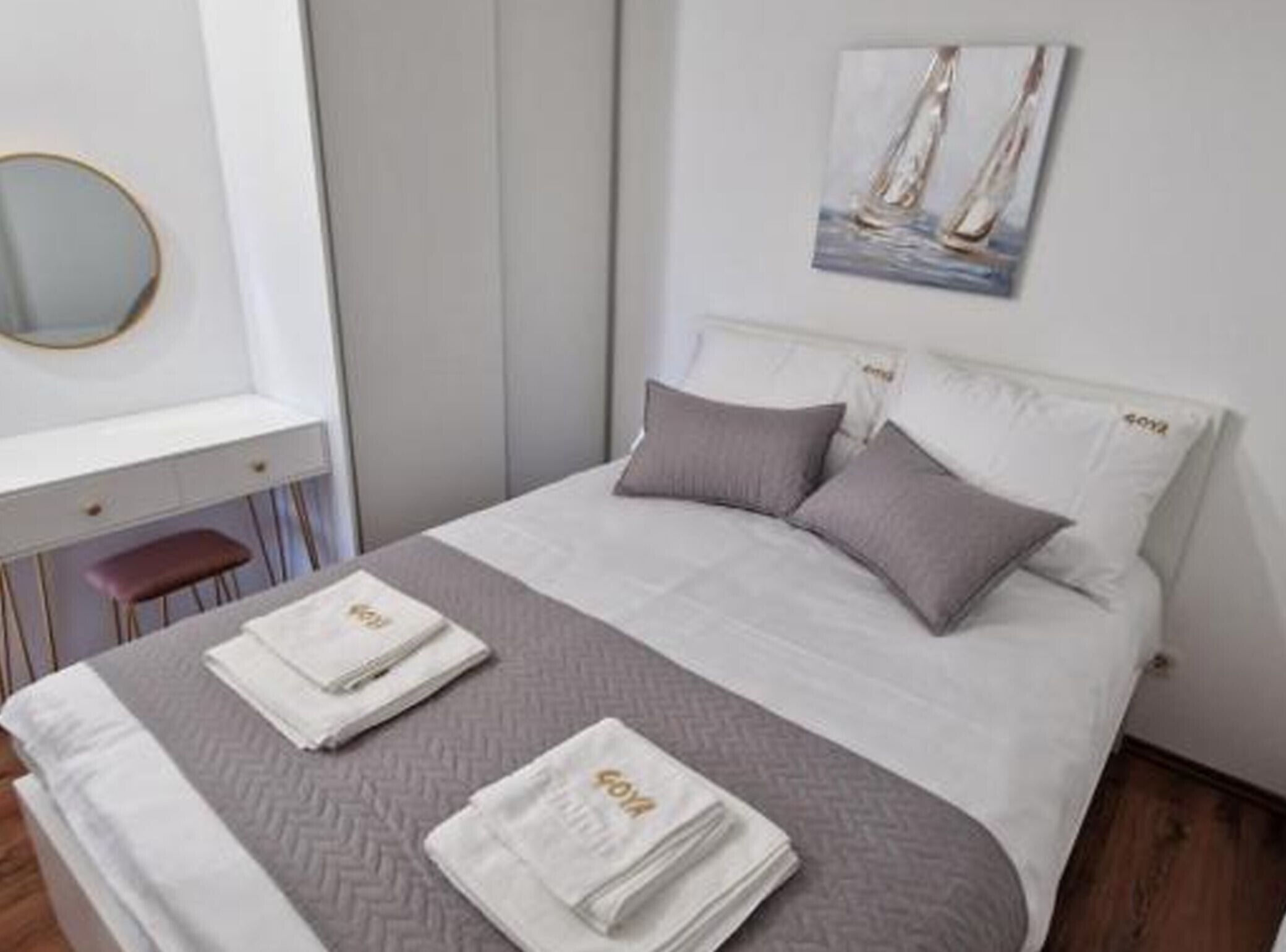 Uma cama bem arrumada com edredom cinza e branco, dois travesseiros e duas toalhas dobradas com um logotipo.
