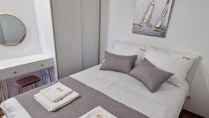 Ein ordentlich bezogenes Bett mit einer grau-weißen Decke, zwei Kissen und zwei gefalteten Handtüchern mit einem Logo.