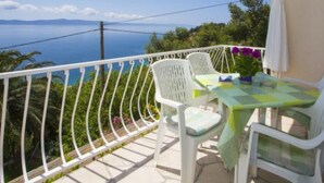 En balkon med hvide stole og et bord, med udsigt over et smukt havlandskab.