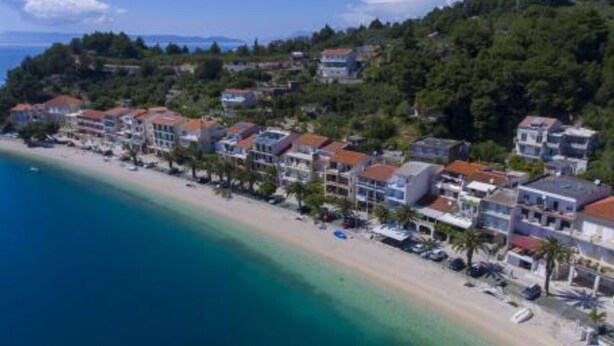 Eine Küstenstadt mit Häusern am Strand, klarem blauen Wasser und einer hügeligen Kulisse.