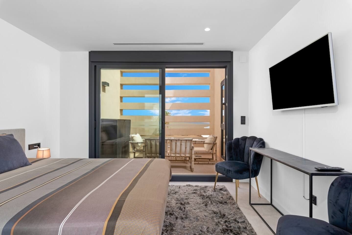 A modern hotel room with a bed, a TV, a desk, and a balcony with a view.
