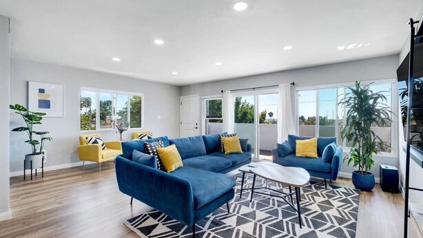A spacious living room with a blue sofa set, yellow chairs, a coffee table, and a patterned rug.