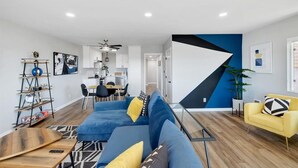 A modern living room with a blue sofa, yellow cushions, a yellow armchair, and a wooden coffee table.