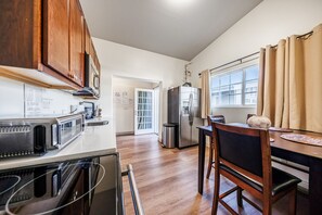 A kitchen with wooden cabinets, a refrigerator, a microwave, and a dining area with a table and chairs. - Welcoming and Spacious 2-Bedroom Suite in Central Torrance, California (Torrance)