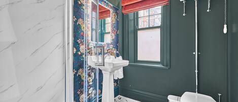 A bathroom with a marble wall, a white pedestal sink, a toilet, and a shower with a glass door.