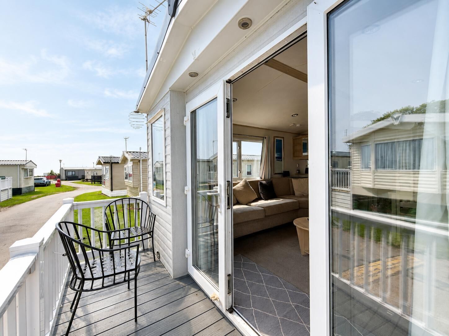 Black metal chairs sit on the grey wooden front decking, with white railings and views of neighbouring caravans.
