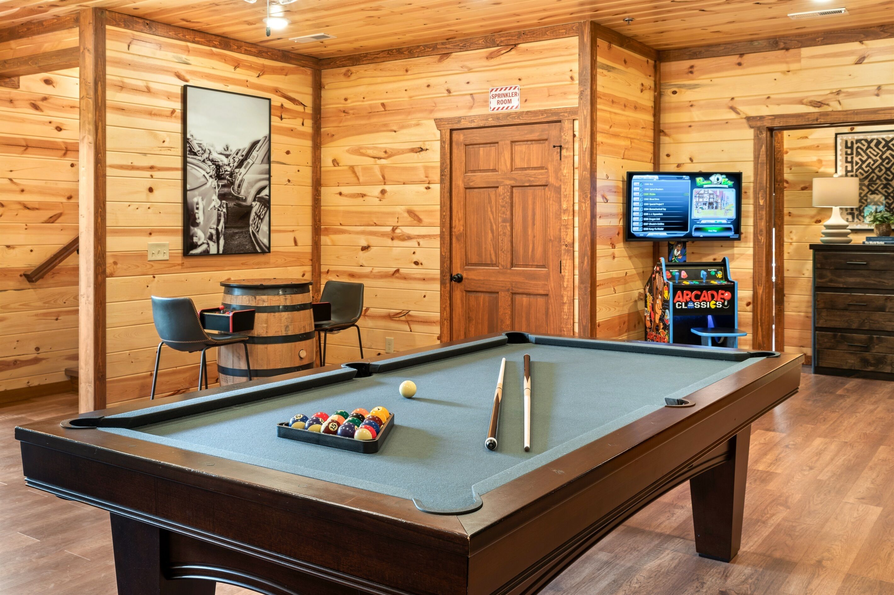 A pool table with a cue stick and balls, a television screen, and a sign indicating a sprinkler system.