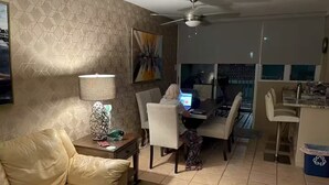 Un salon avec un canapé, une table basse, une lampe et un chien. Il y a également un coin repas avec une table et des chaises.