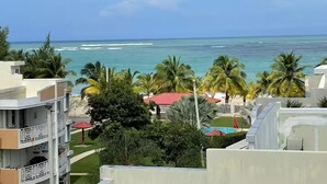Un hôtel situé en bord de mer, doté de nombreux balcons, de palmiers et offrant une vue sur l’océan.