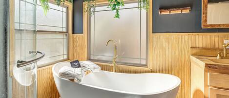 Un bagno moderno con una vasca freestanding, rivestimenti in legno e piante sospese.