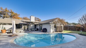 Una casa moderna con piscina, mobiliario de exterior y porche cubierto.