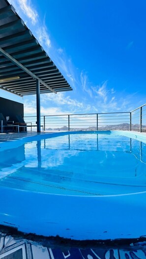 Une piscine à débordement offrant une vue dégagée sur les montagnes en arrière-plan, un espace abrité avec des sièges et une rambarde métallique entourant la piscine.