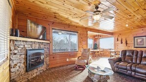 Ein gemütliches Blockhaus-Interieur mit Kamin aus Stein, Holzwänden, einer Ledersofa und einem Glastisch.