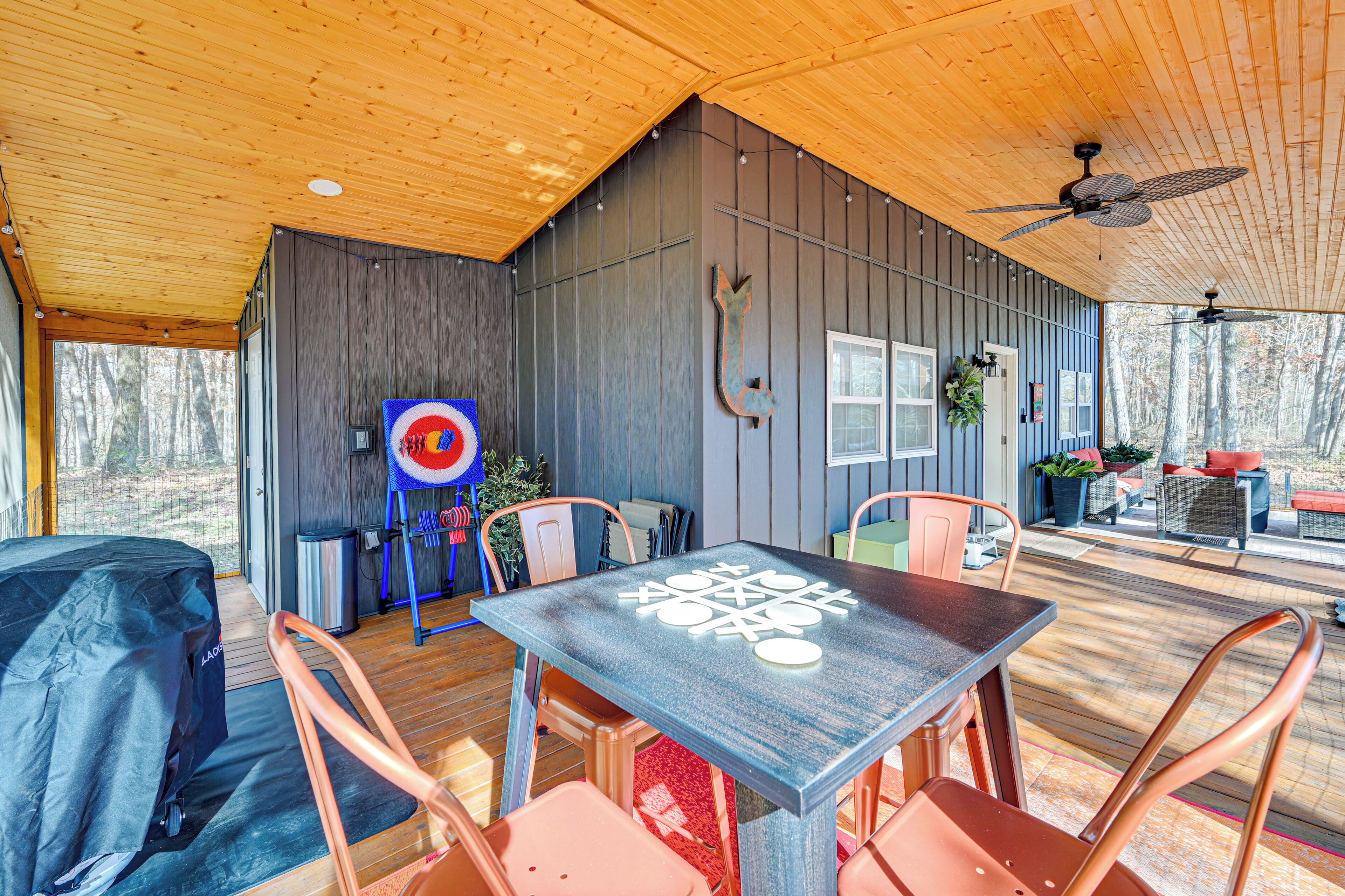 A covered patio area with a table and chairs, a ceiling fan, and a view of the surrounding forest.