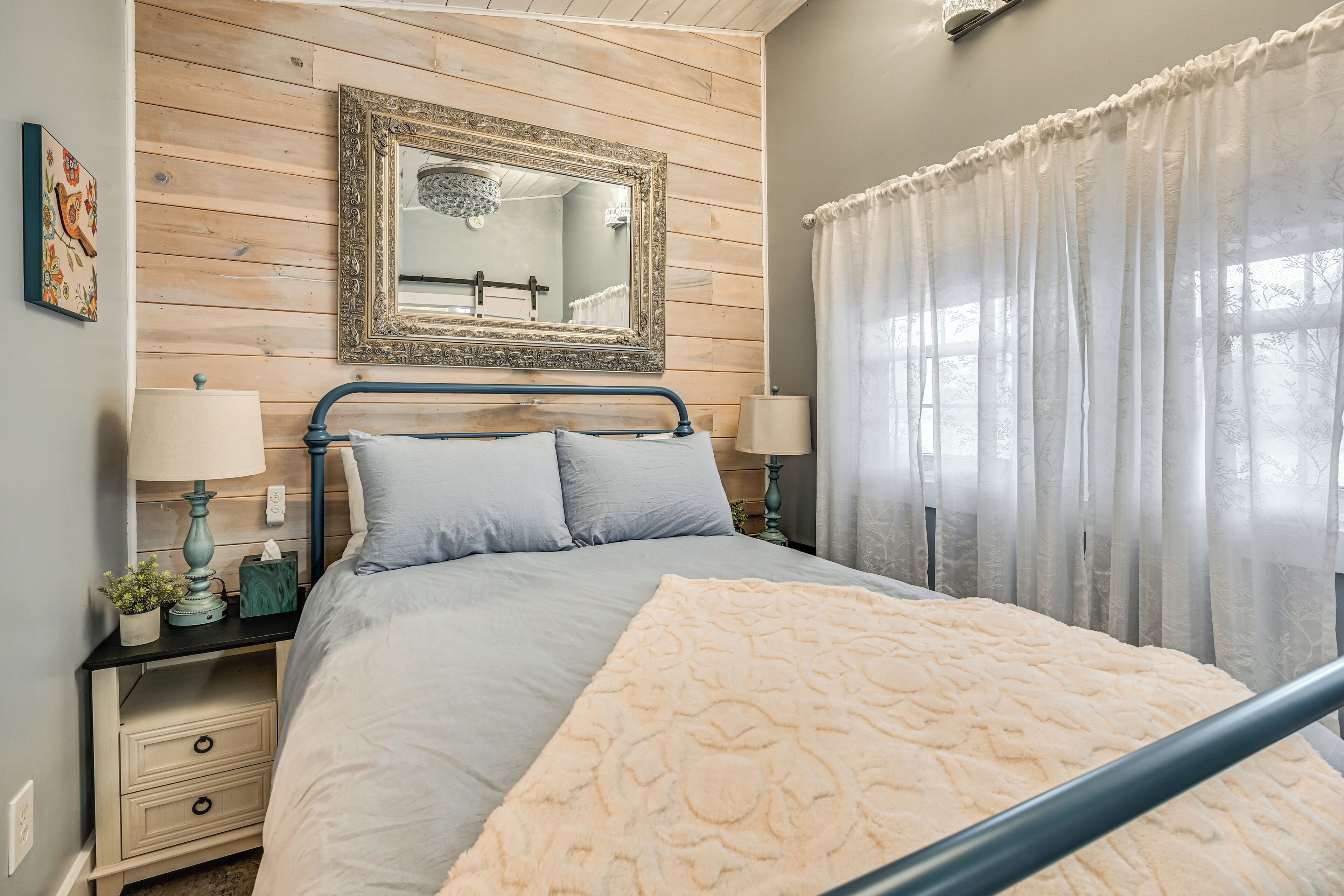 A bedroom with a bed, nightstands, a mirror, and a window with curtains.