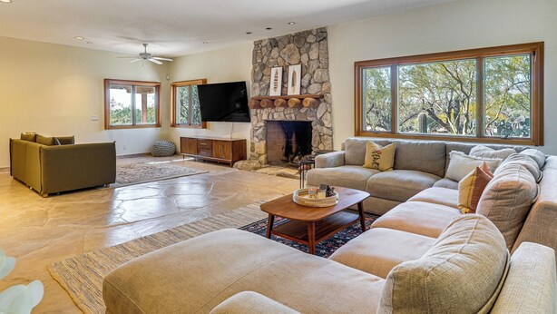 A spacious living room with a stone fireplace, large windows, and a flat-screen TV mounted above it. - Private Casita in the Foothills of Mt Lemmon! (Tucson)