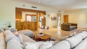 A spacious living room with a large grey sofa, a coffee table, and a dining area with wooden chairs and a kitchen in the background. - Private Casita in the Foothills of Mt Lemmon! (Tucson)