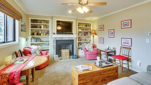 A cozy living room with a fireplace, bookshelves, a dining table, and a ceiling fan. - 6 Mi to Dtwn Fort Collins: Cozy Apt w/ Shared Yard (Fort Collins)