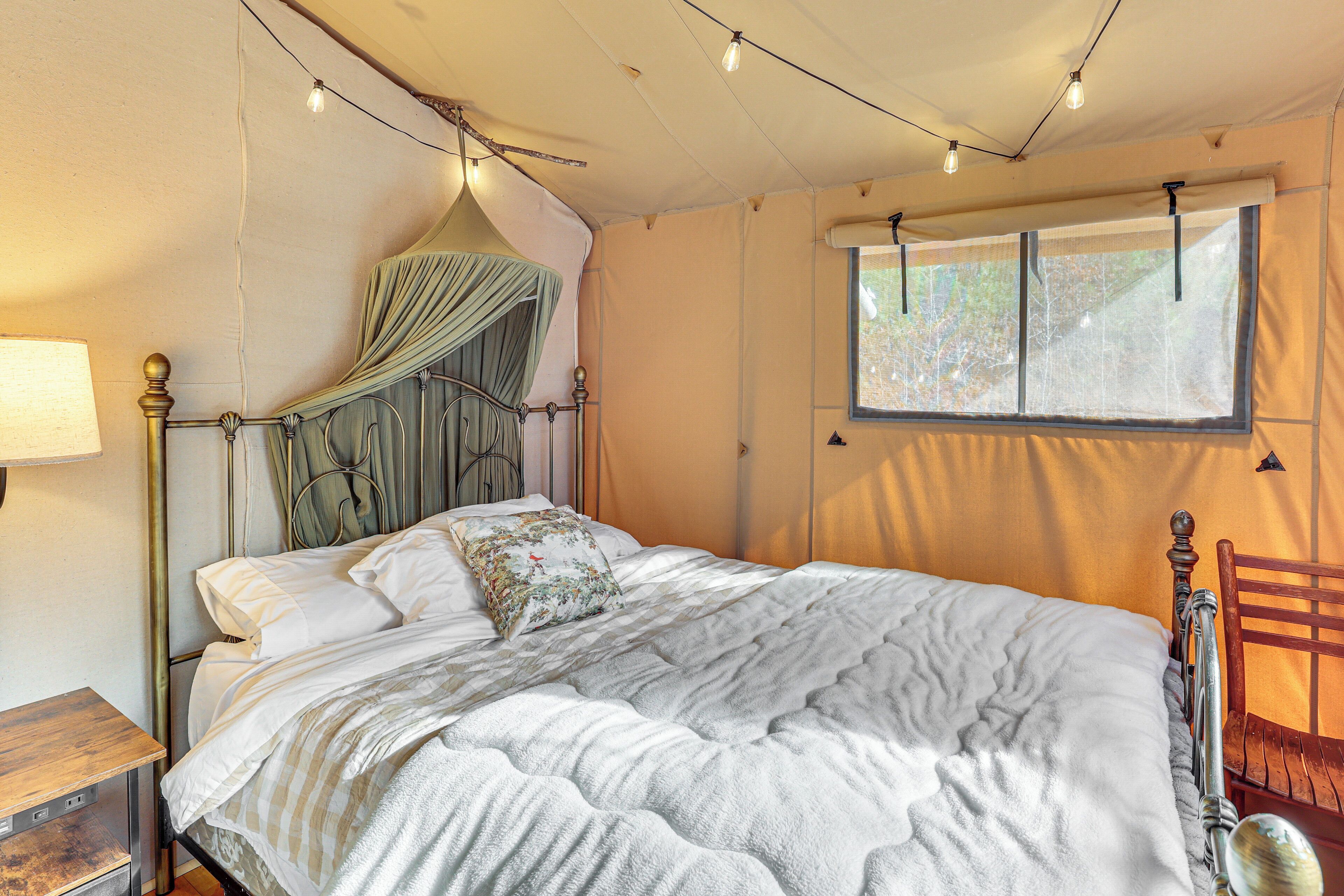 Een bed met hemel, een houten nachtkastje, een raam met uitzicht en een stoel.